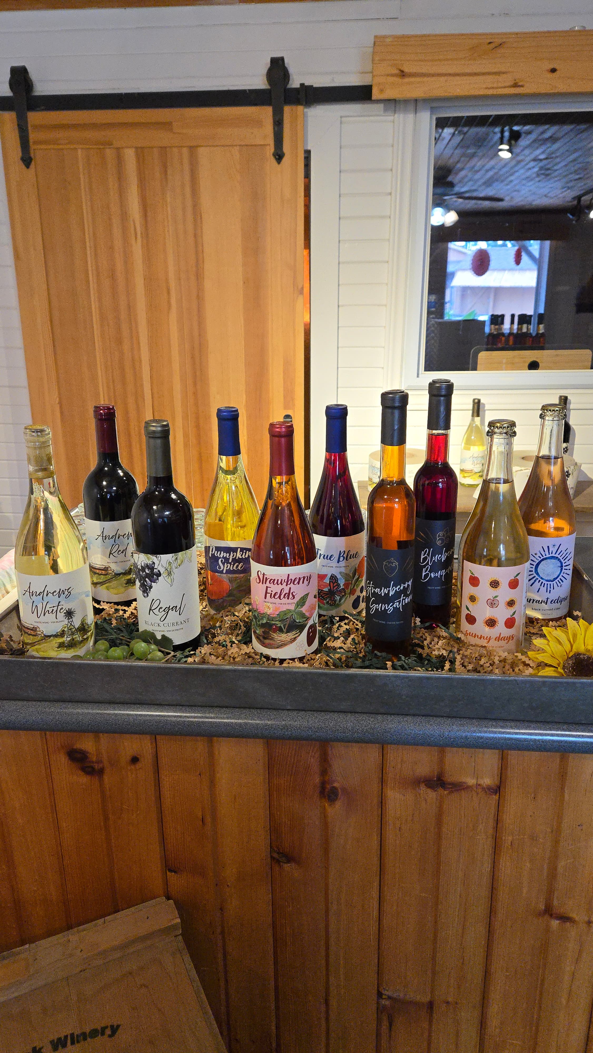 A row of Andrews fruit wine bottles, including Strawberry Fields, True Blue, Regal Black Currant and Strawberry Sensation, lined up on the winery counter