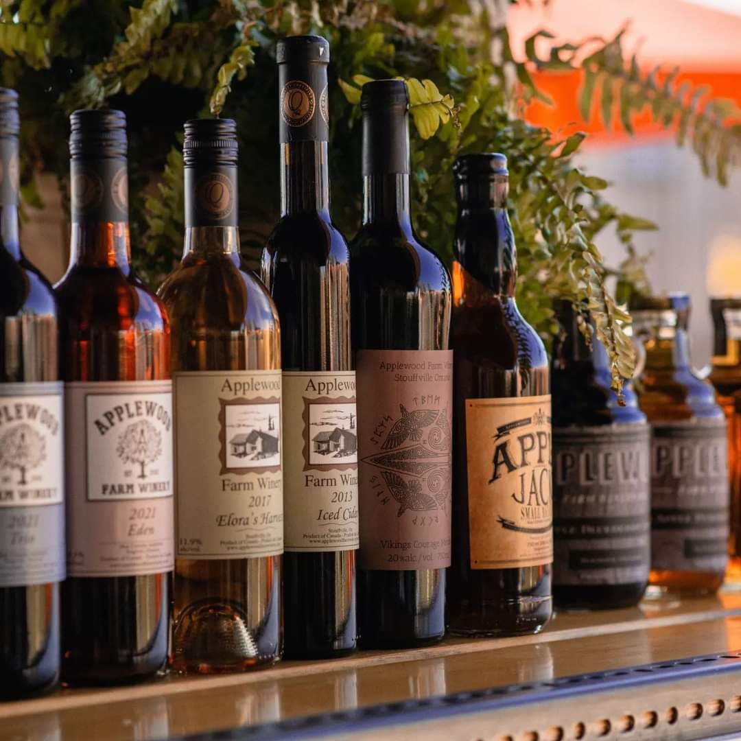 A row of Applewood Farm Winery bottles on a bar, including Trio, Eden, Elora's Harvest, Iced Cider and Apple Jack