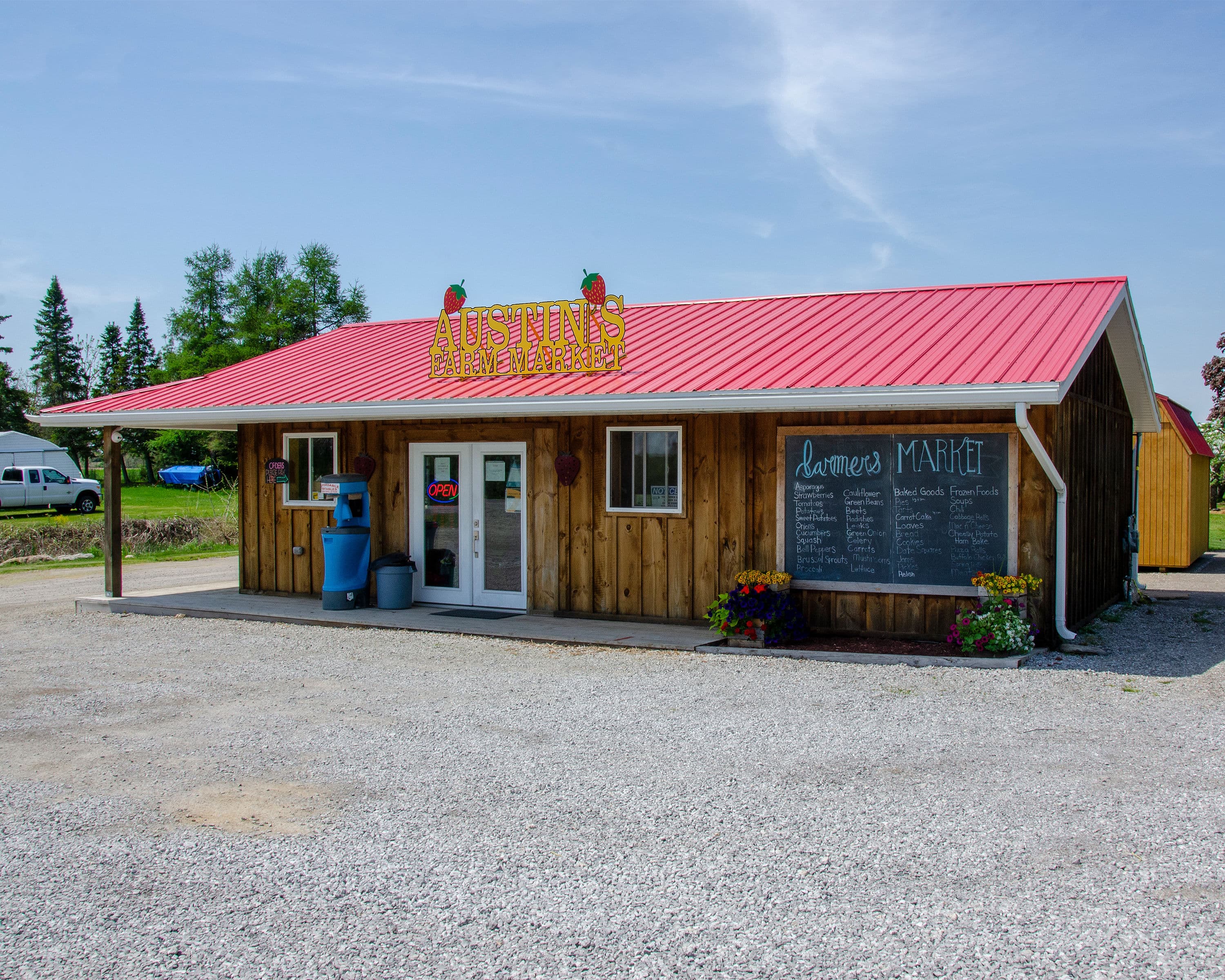 Austin's Farm Market, a board-and-batten building with a red roof, strawberry sign and a chalkboard listing produce, baking and frozen foods