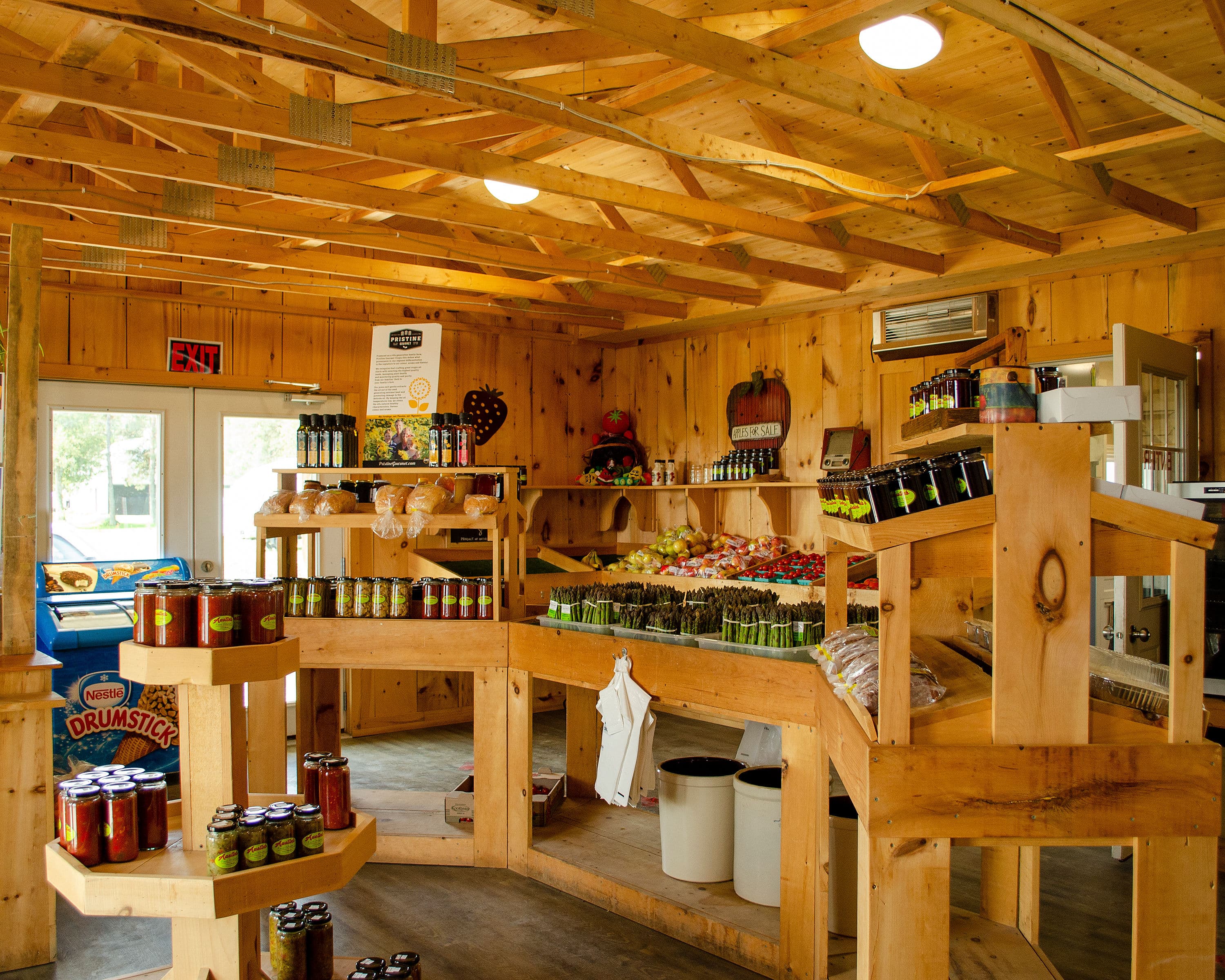 Inside Austin's farm market: wooden shelves of asparagus bundles, apples, bread, and jars of salsa and pickles with the farm's own labels