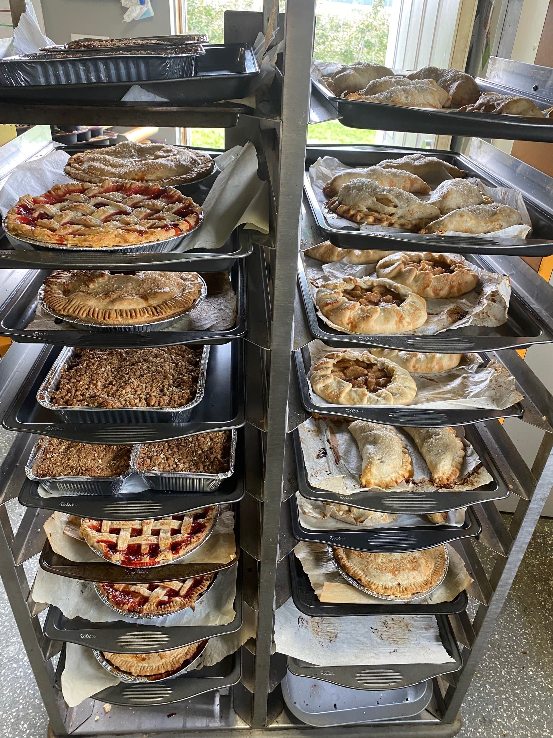 A tall bakery rack filled with lattice pies, galettes and trays of apple crisp in the Brantview scratch bakery
