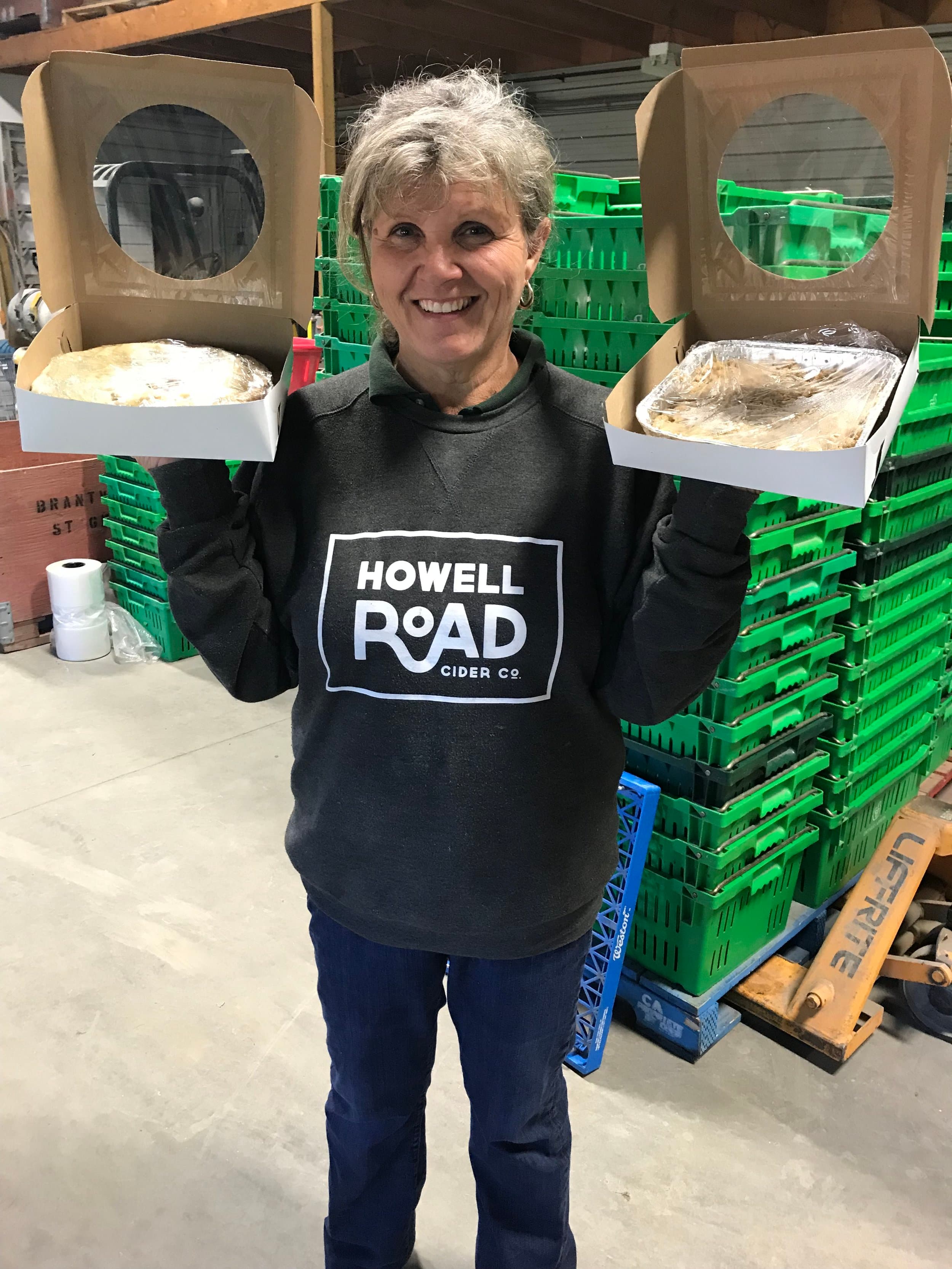Linda Howell, the farm's baker, smiling in a Howell Road sweatshirt and holding up two boxed pies in the packing barn