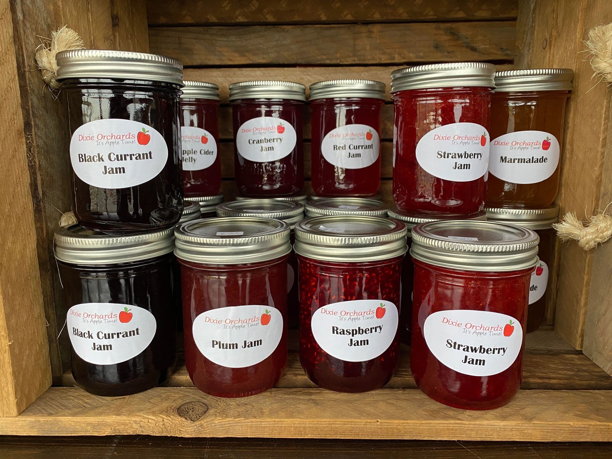 Jars of Dixie Orchards black currant, plum, raspberry and strawberry jam stacked in a wooden crate