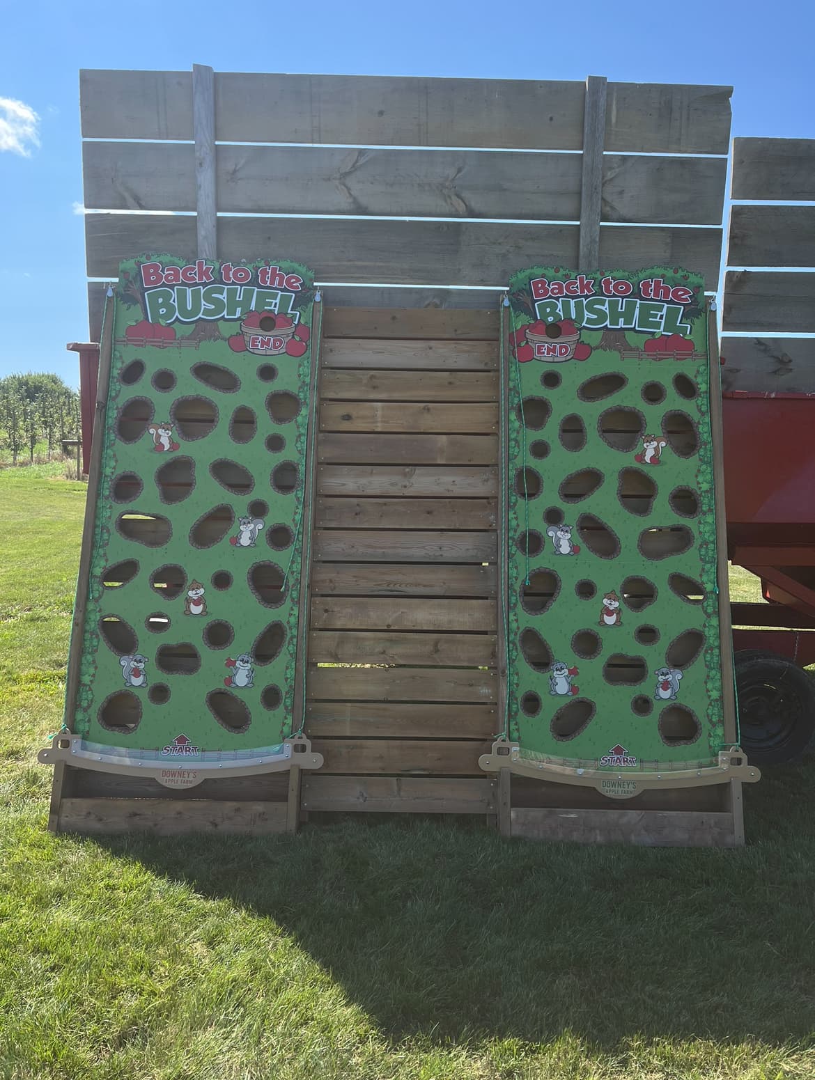 Two Back to the Bushel ball-run boards with the Downey's Apple Farm name, propped against the side of a wooden hay wagon on the grass