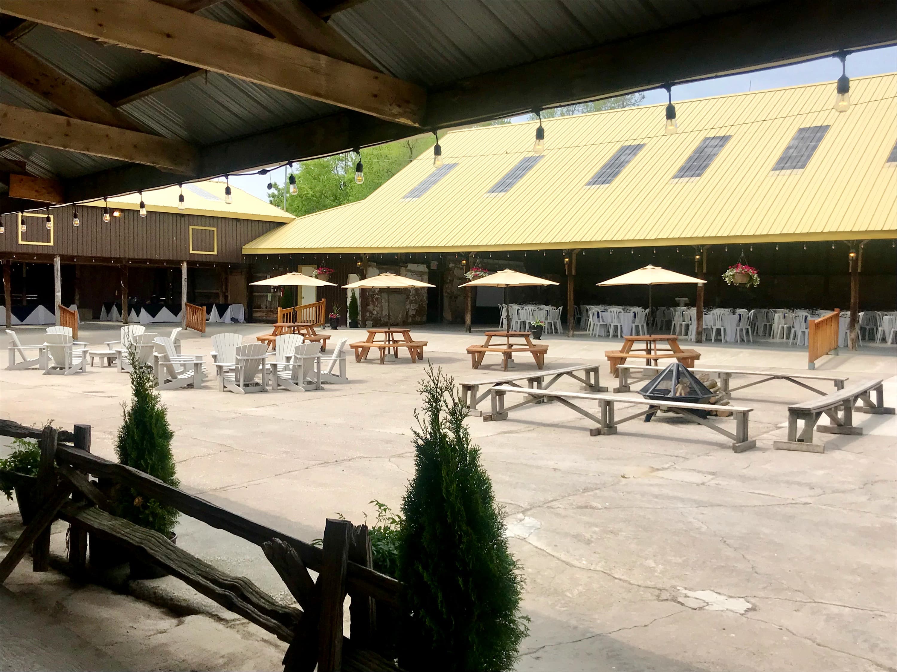 The barn courtyard with picnic tables, umbrellas, Muskoka chairs and a fire pit, framed by a split-rail fence and the yellow-roofed barns