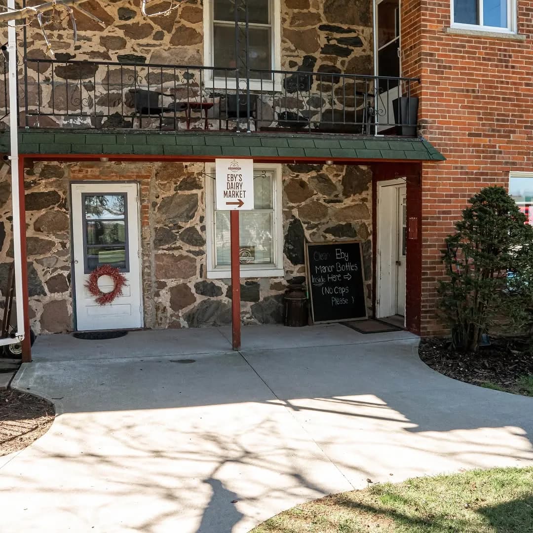 The stone and brick entrance to Eby's Dairy Market, with its hanging sign and a chalkboard about returning bottles