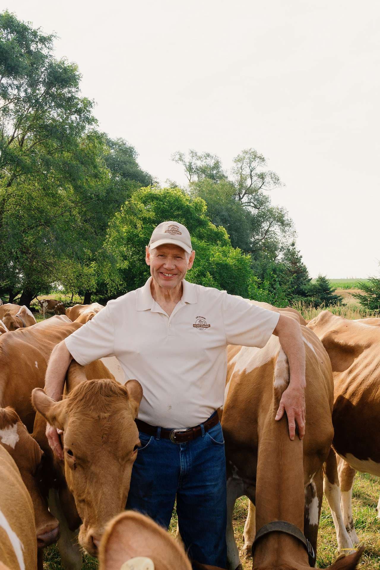 Jim Eby smiling among his Guernsey cows in a summer pasture at Eby Manor Farm