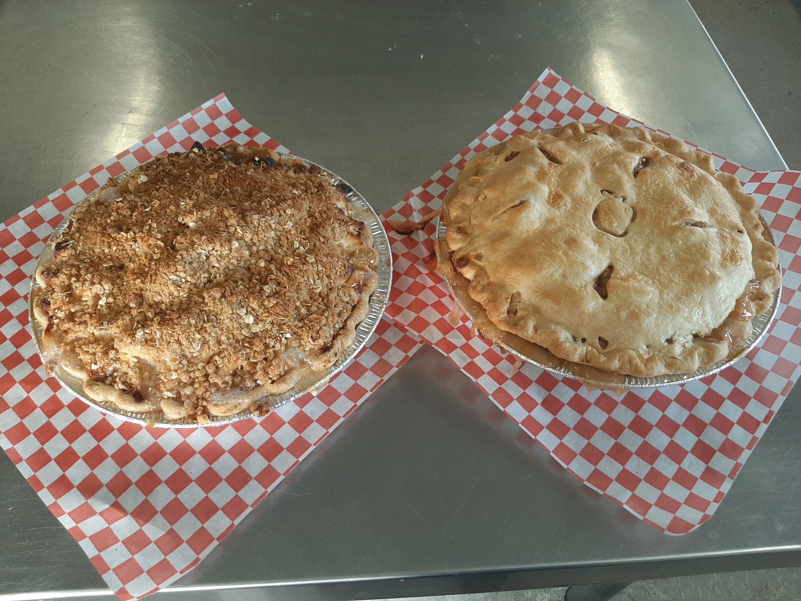 An apple crumble pie and a double-crust apple pie side by side on red-and-white checked paper