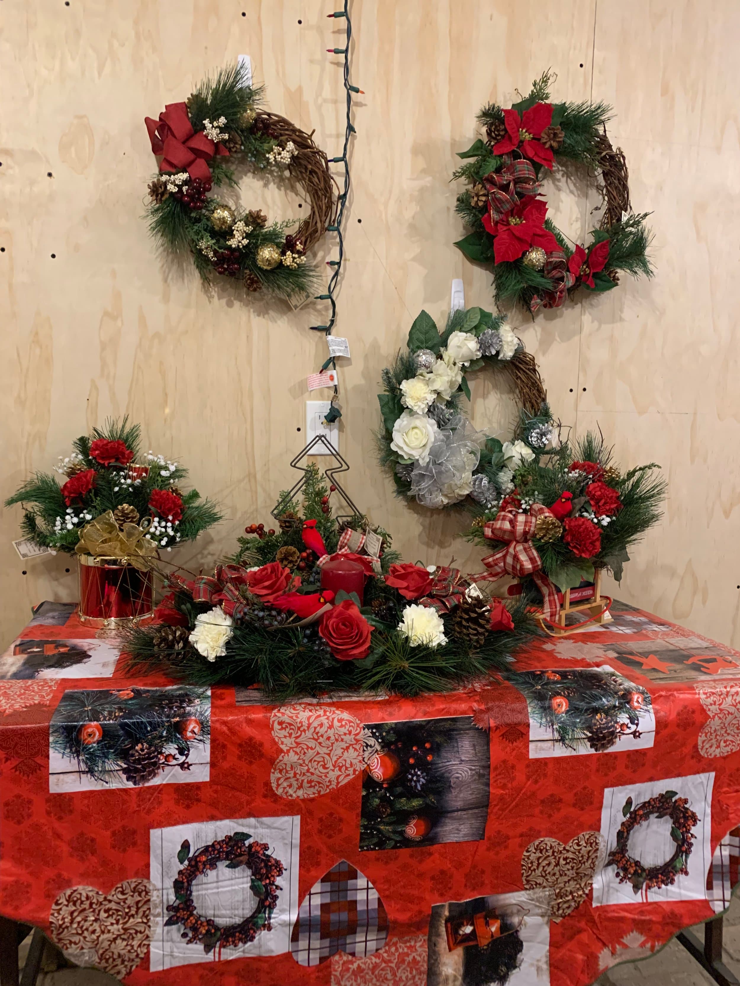 Christmas wreaths of poinsettias, roses and pine cones hung on a plywood wall above a table of red rose and pine centrepieces