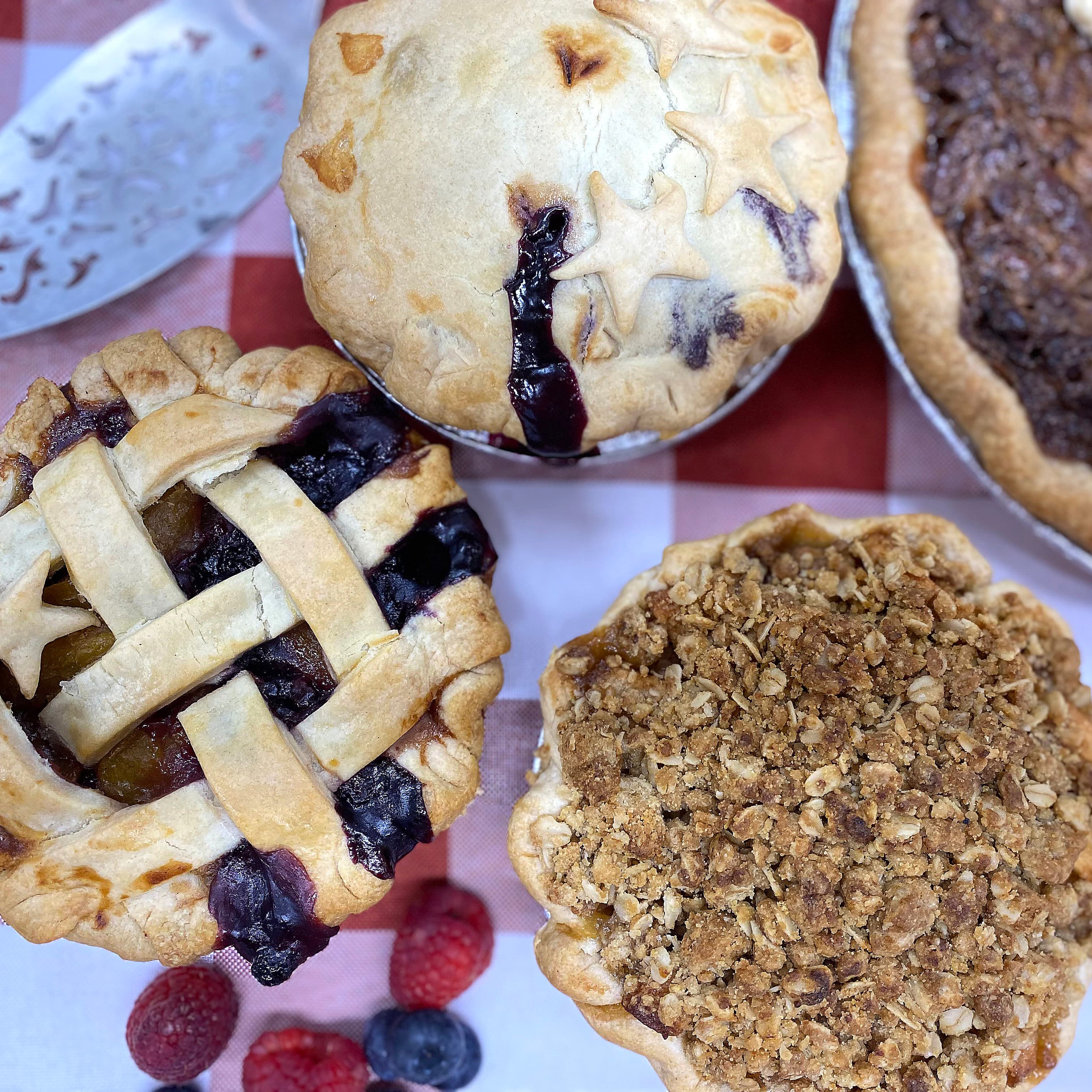 Blueberry, lattice-top, crumble and pecan pies on a red checked cloth, with fresh raspberries and blueberries