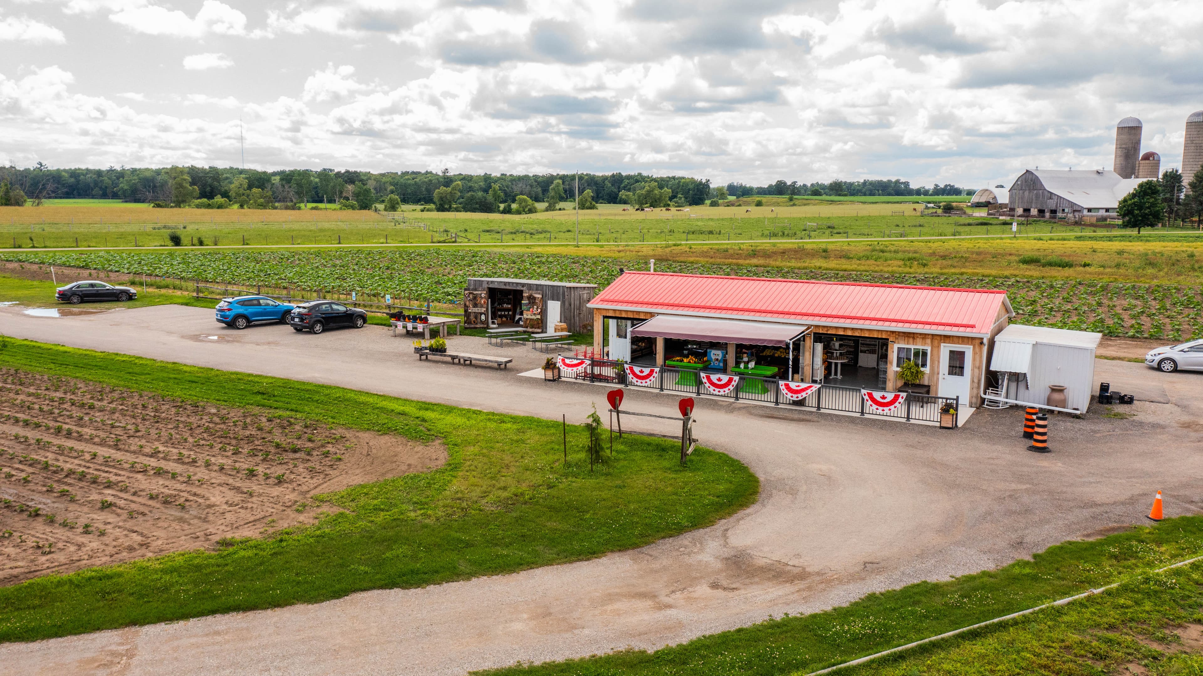 Aerial view of the red-roofed Moore Farms store on its gravel lane, with crop fields, barns and silos behind