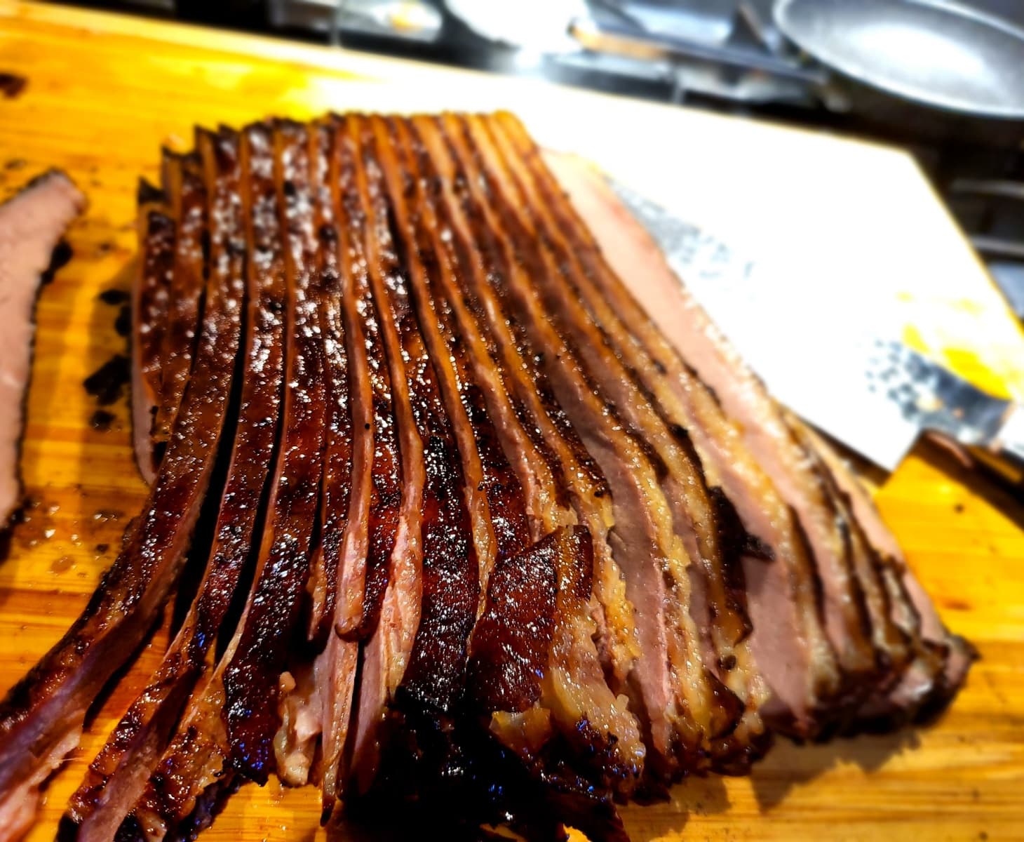 Slices of smoked beef brisket with a dark crust fanned out on a wooden cutting board beside a cleaver