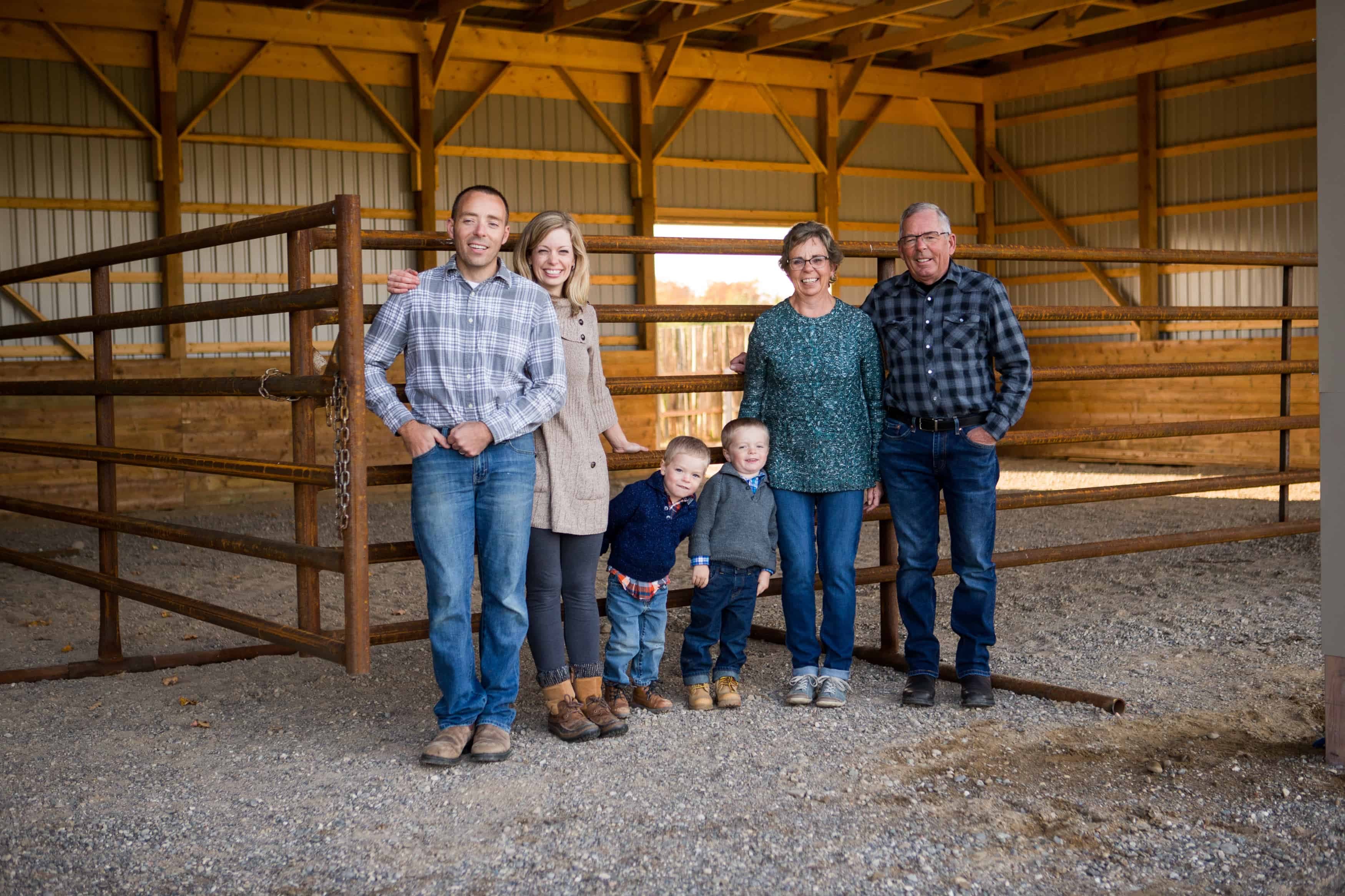 Three generations of the Murphy family, two young boys among them, smiling together in an open-sided barn with steel cattle gates at Murphy Meadow Farms