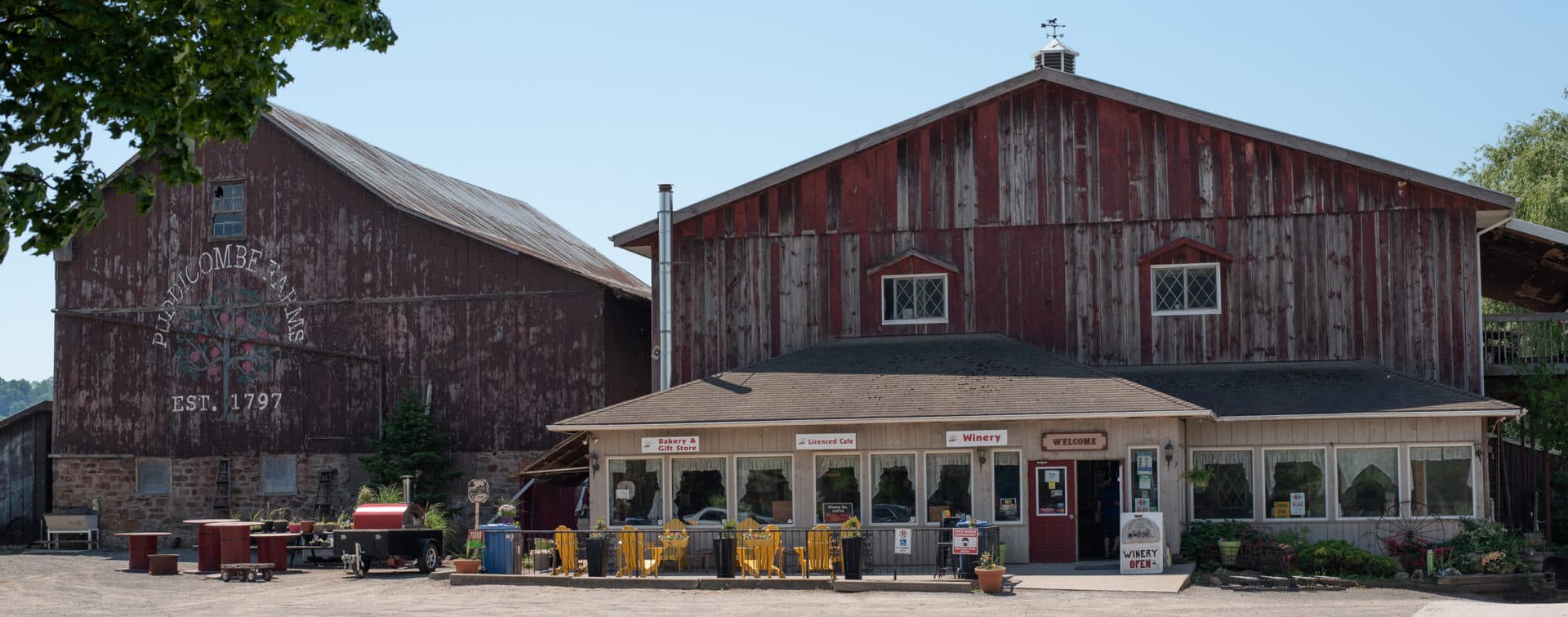 Two weathered red barns, one painted with Puddicombe Farms Est. 1797, and the bakery, licensed cafe and winery storefront with yellow chairs on its porch