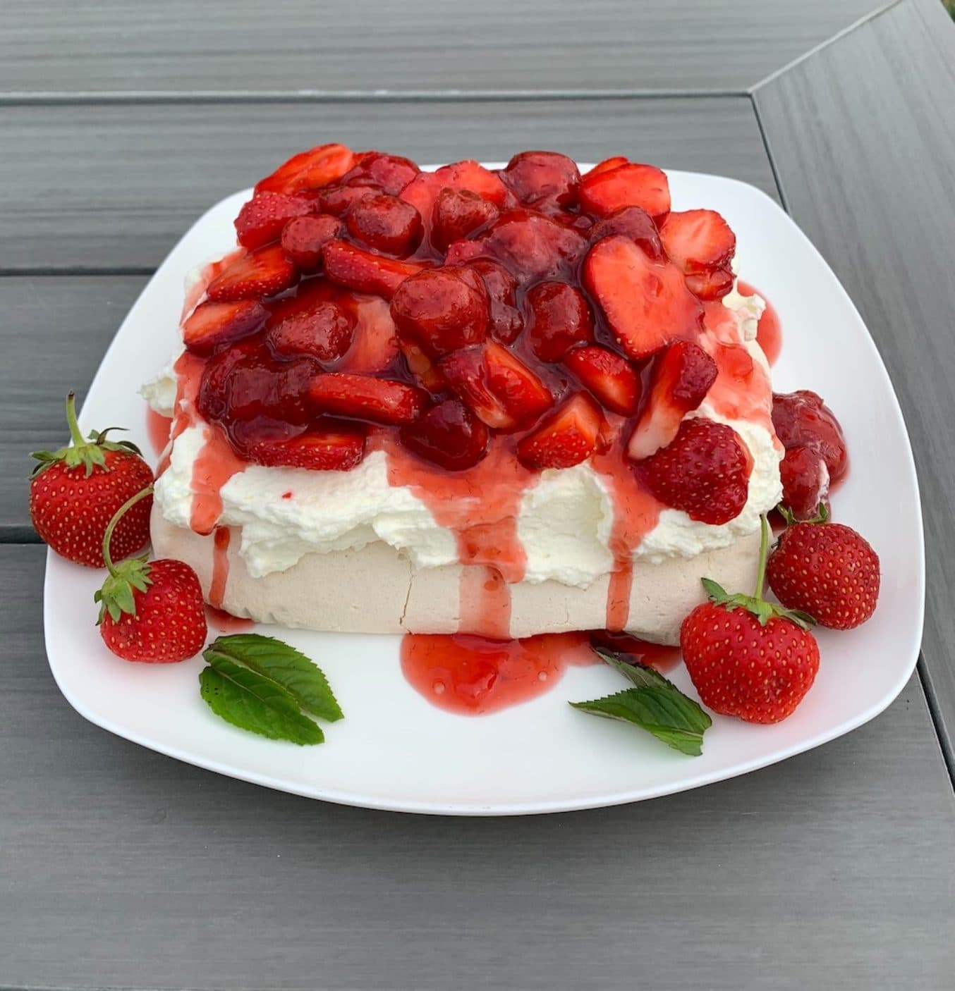 A strawberry pavlova piled with glazed strawberries over whipped cream, with whole berries and mint on the plate