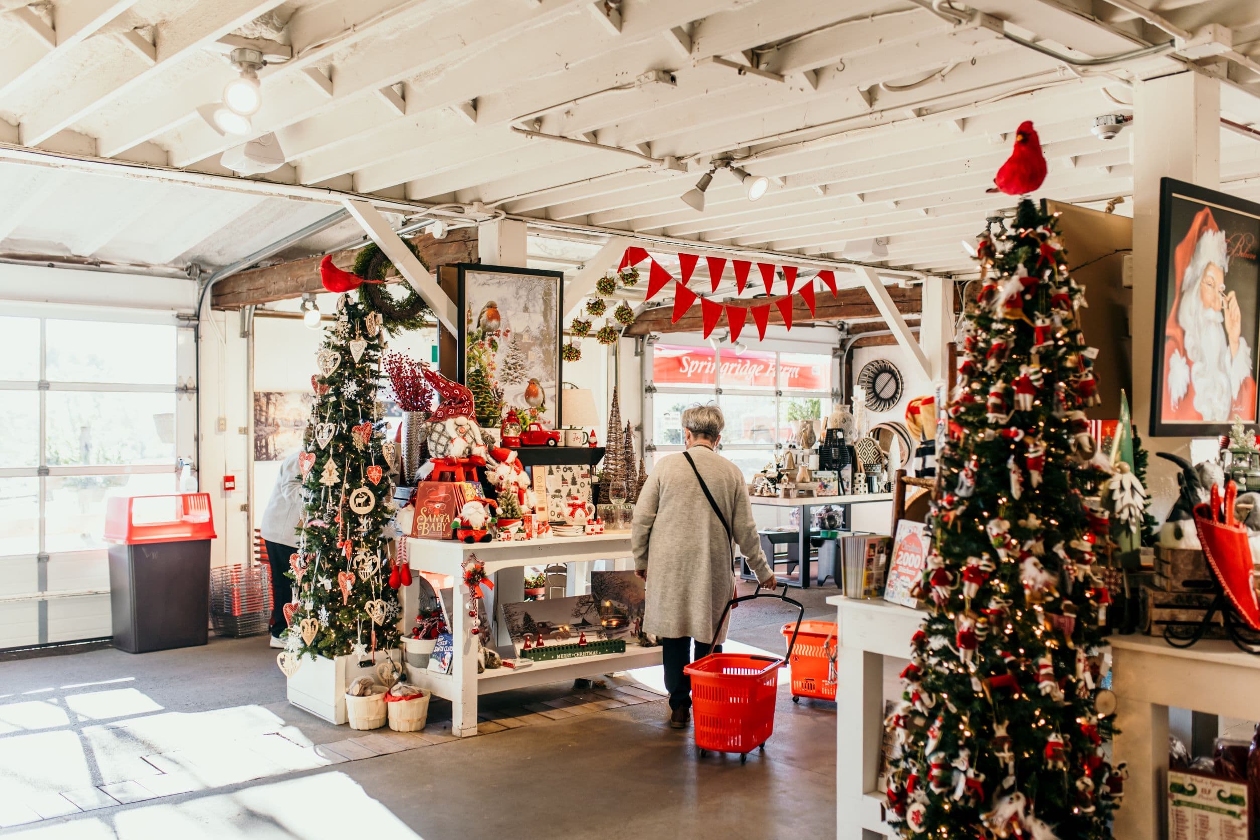 Inside the Barn Market at Christmas: decorated trees, red bunting and gift tables, with a shopper and her red basket seen from behind