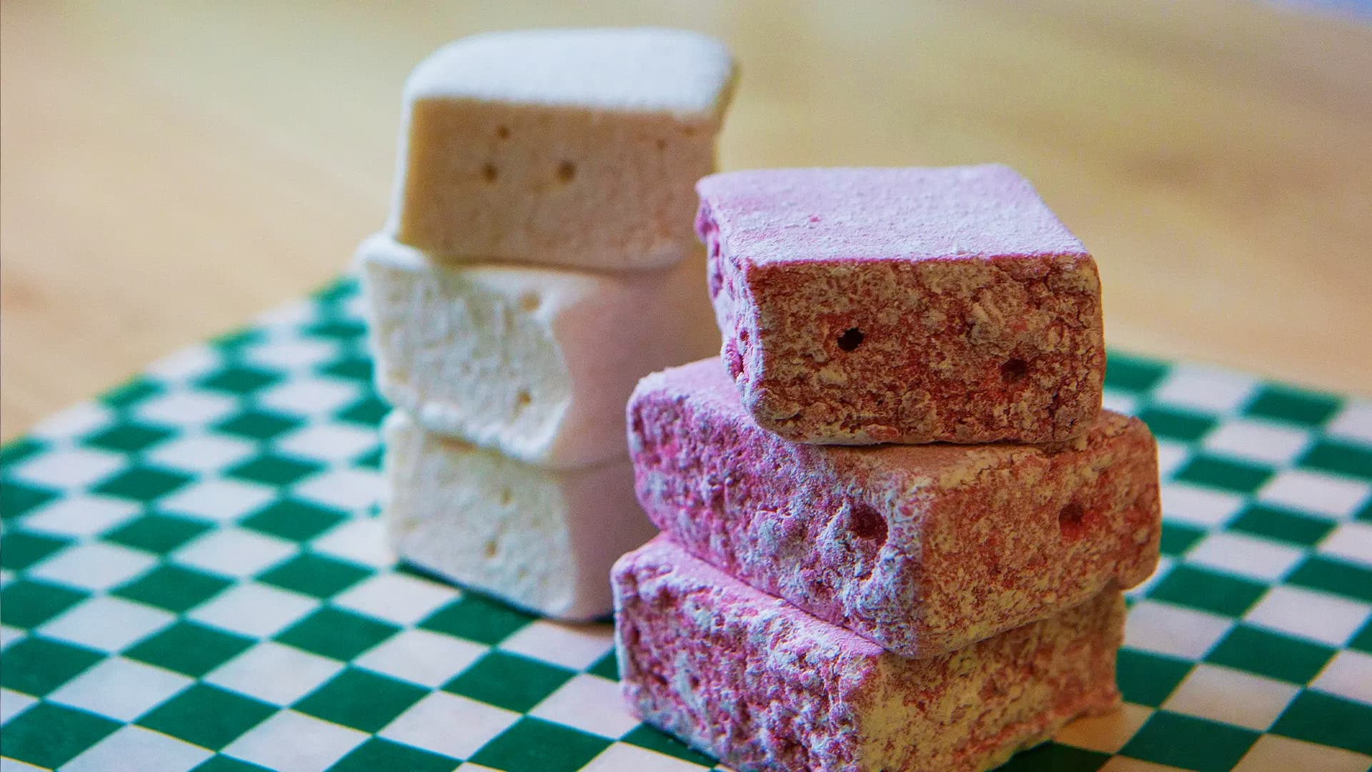 Two stacks of square homemade marshmallows, one plain white and one dusted purple with haskap, on green and white checked paper