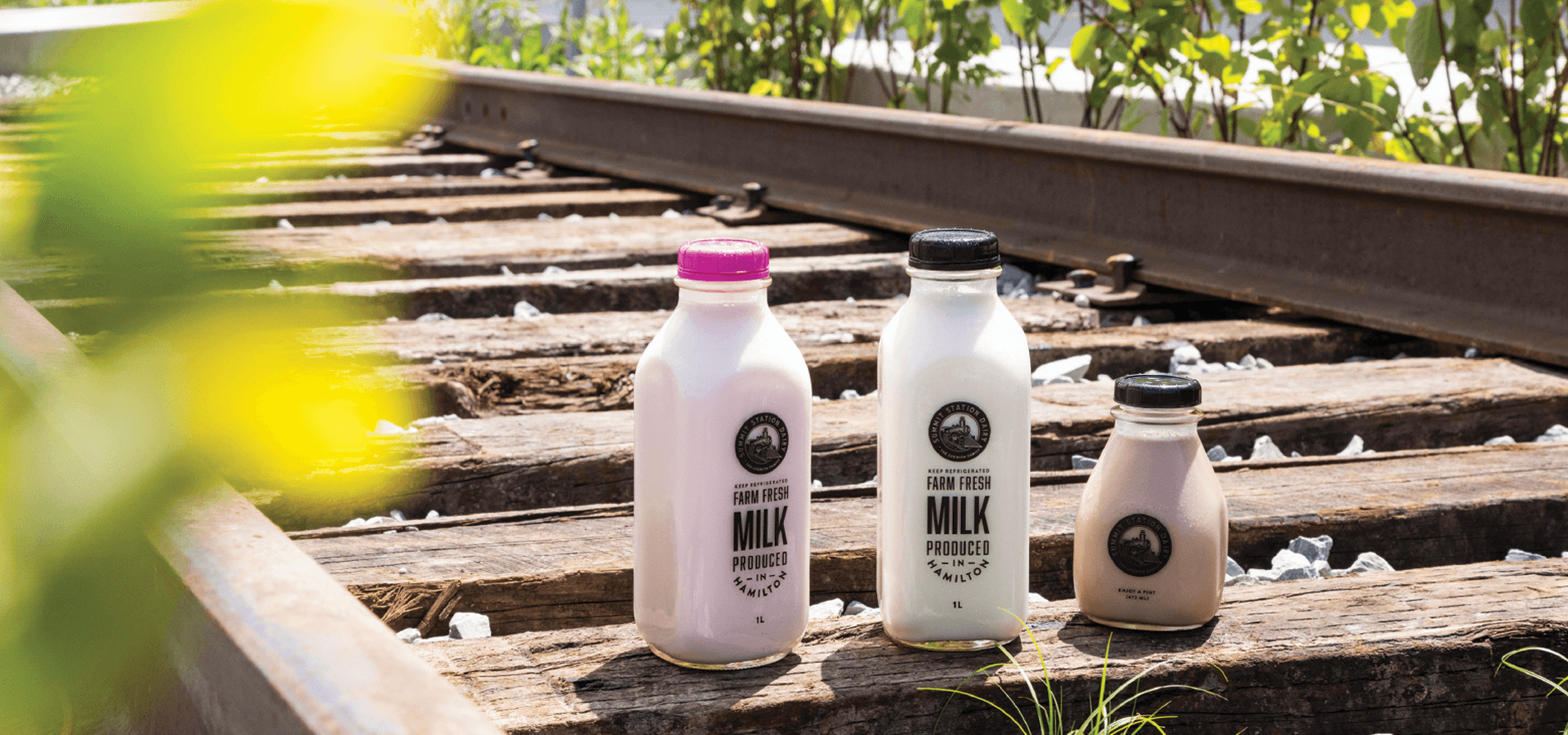 Strawberry, white and chocolate milk in Summit Station glass bottles standing on old railway sleepers in the sun