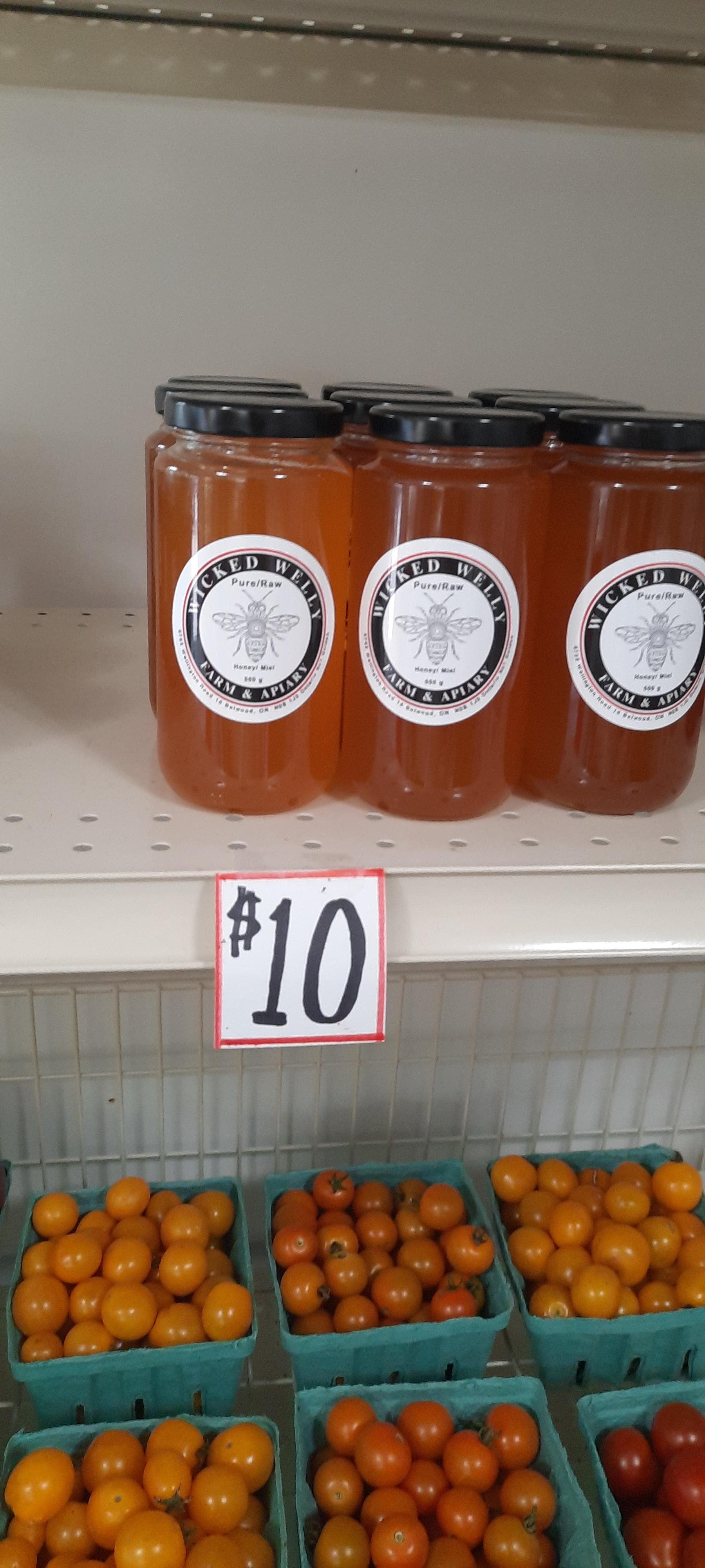 Jars of Wicked Welly pure raw honey on a farm store shelf above pints of orange cherry tomatoes