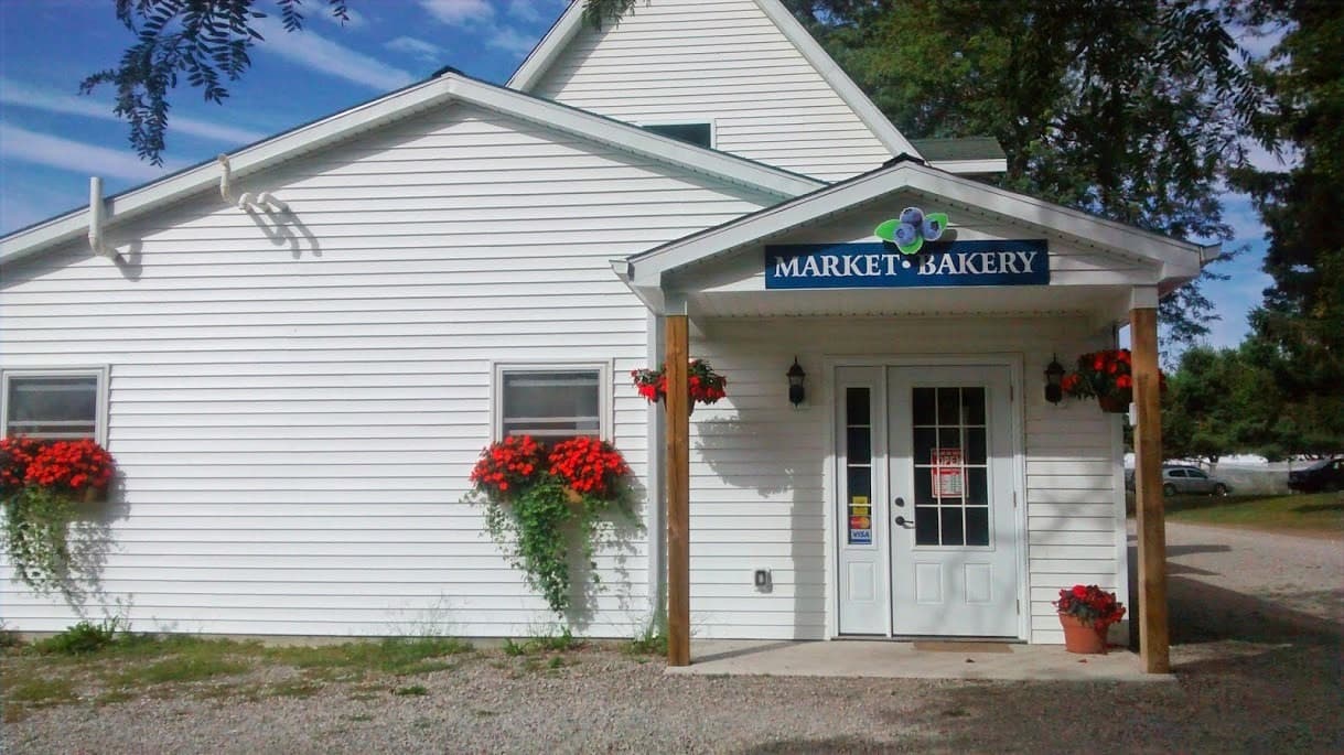 The white farm market building with a Market and Bakery sign over the porch and red flowers in the window boxes