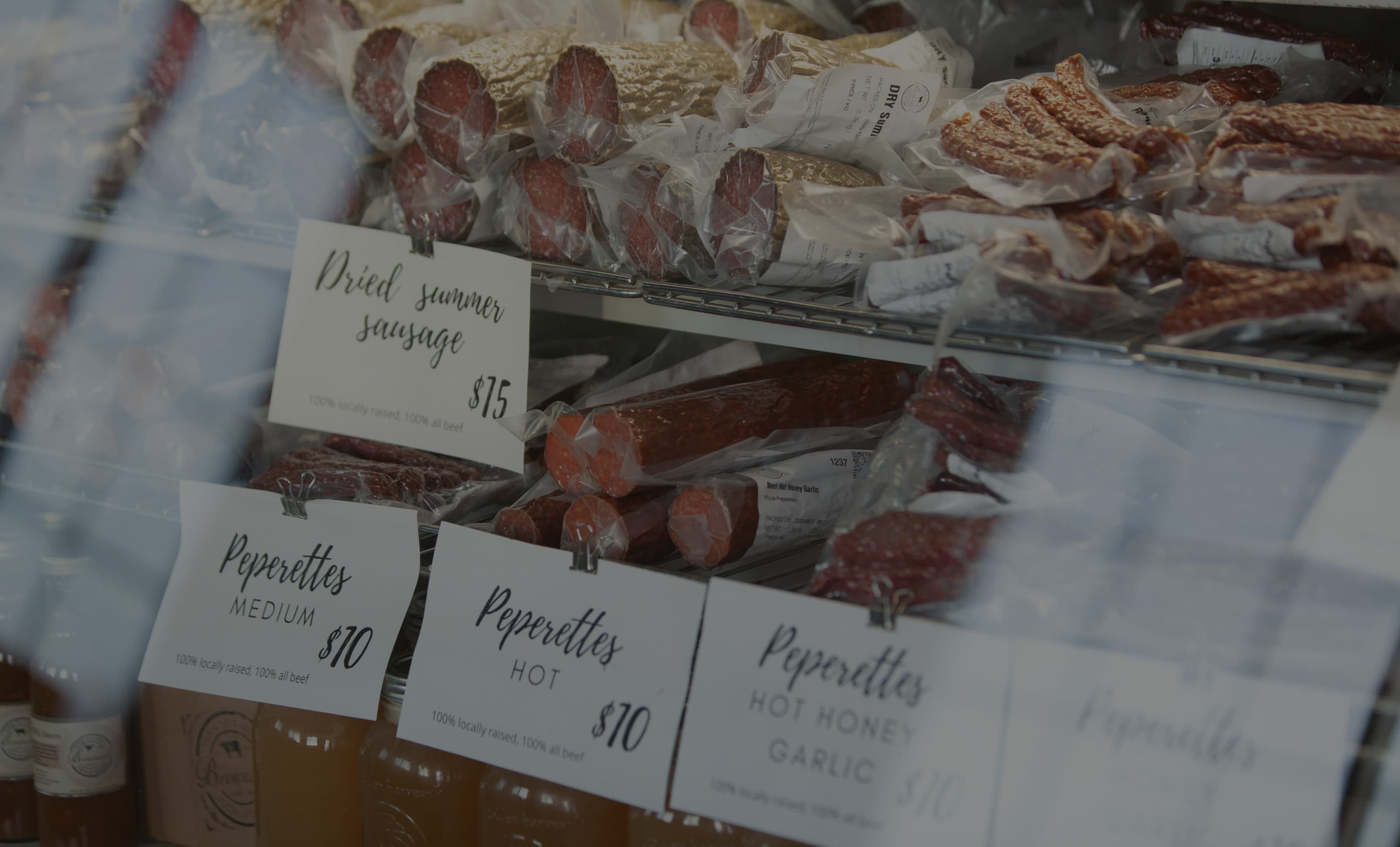 Dried summer sausage and beef pepperettes in the farm store's cooler, with printed price cards