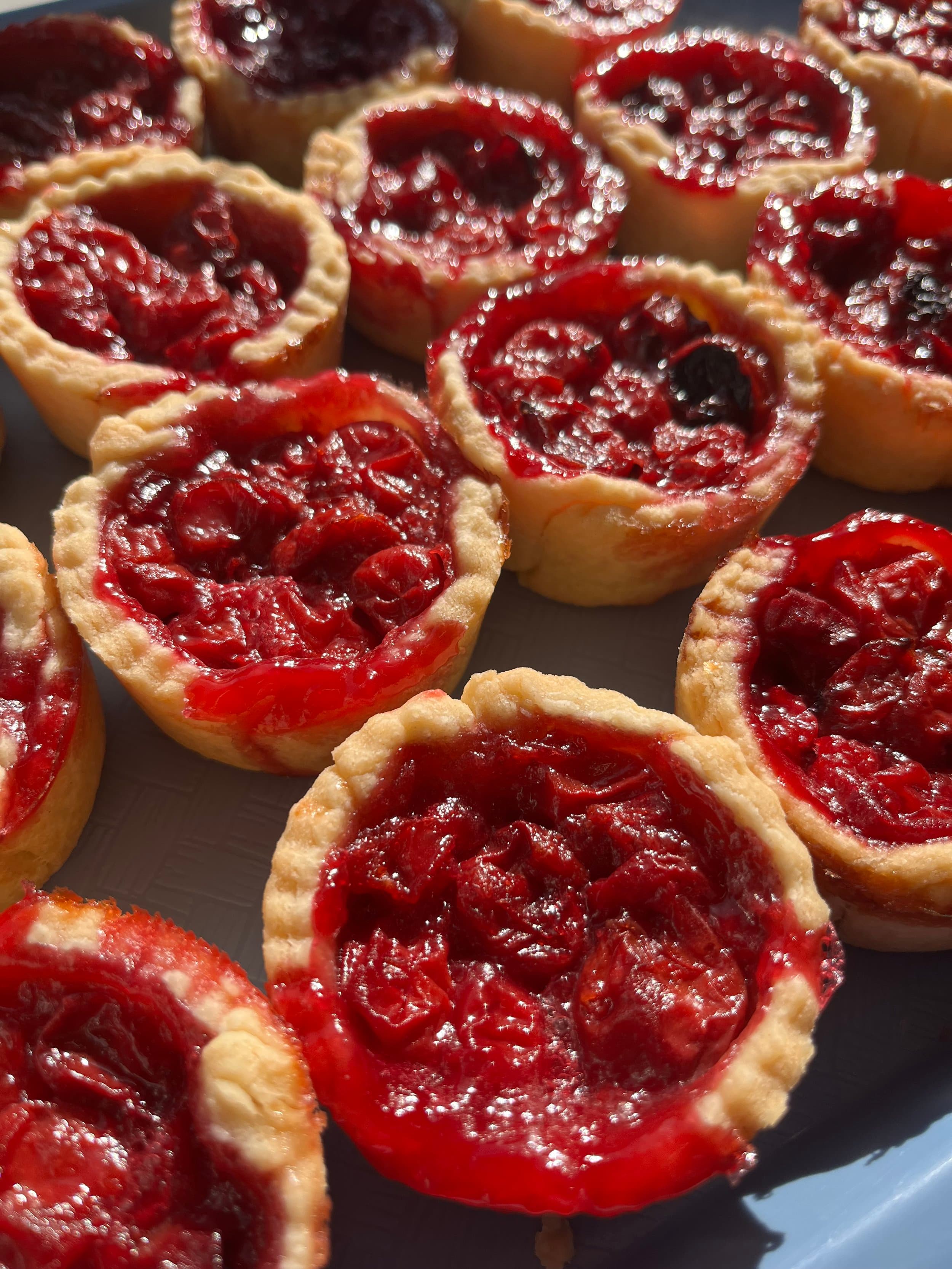 A plate of small cherry tarts with crimped pastry and glossy fruit filling in the sun