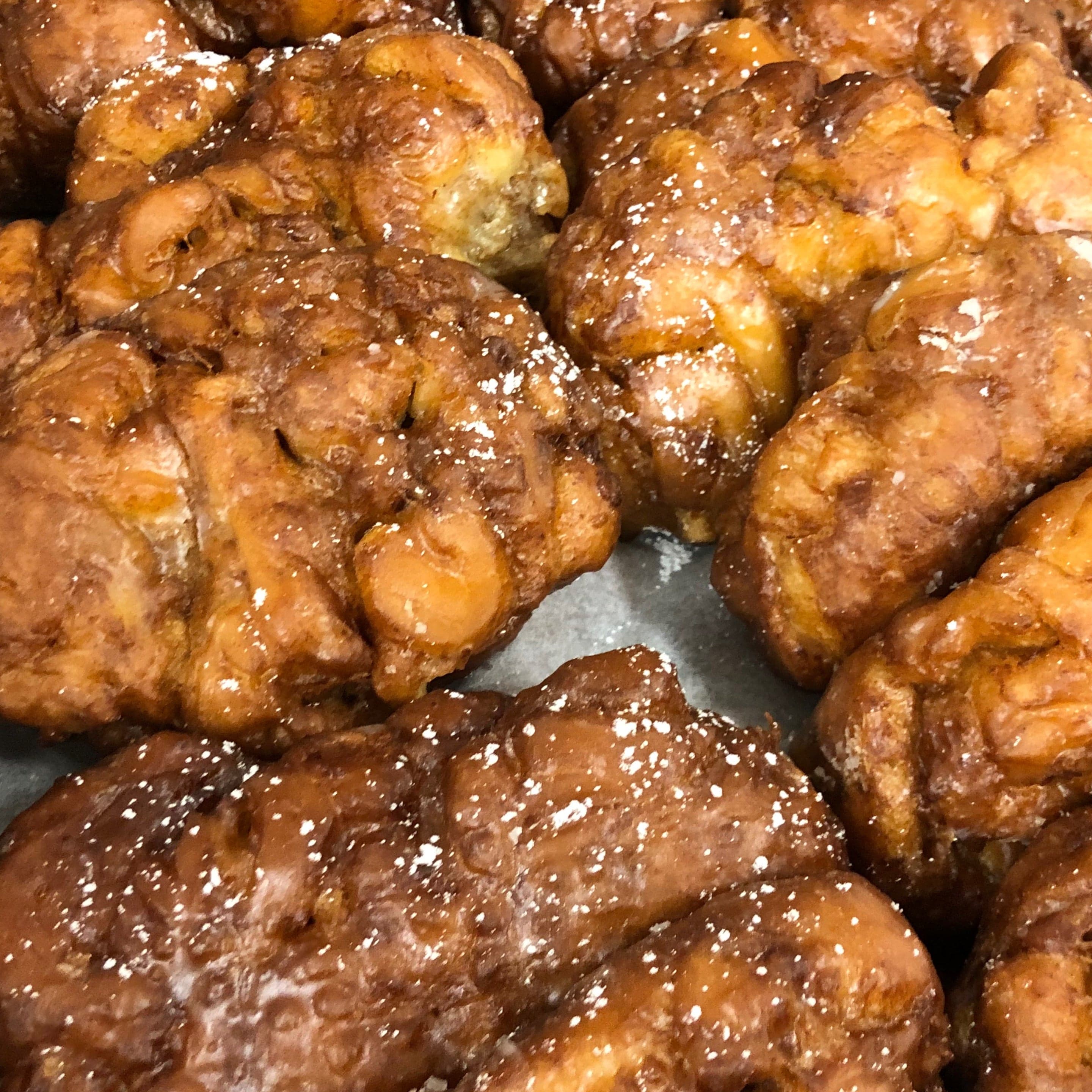 A tray of glazed apple fritters dusted with icing sugar, close up