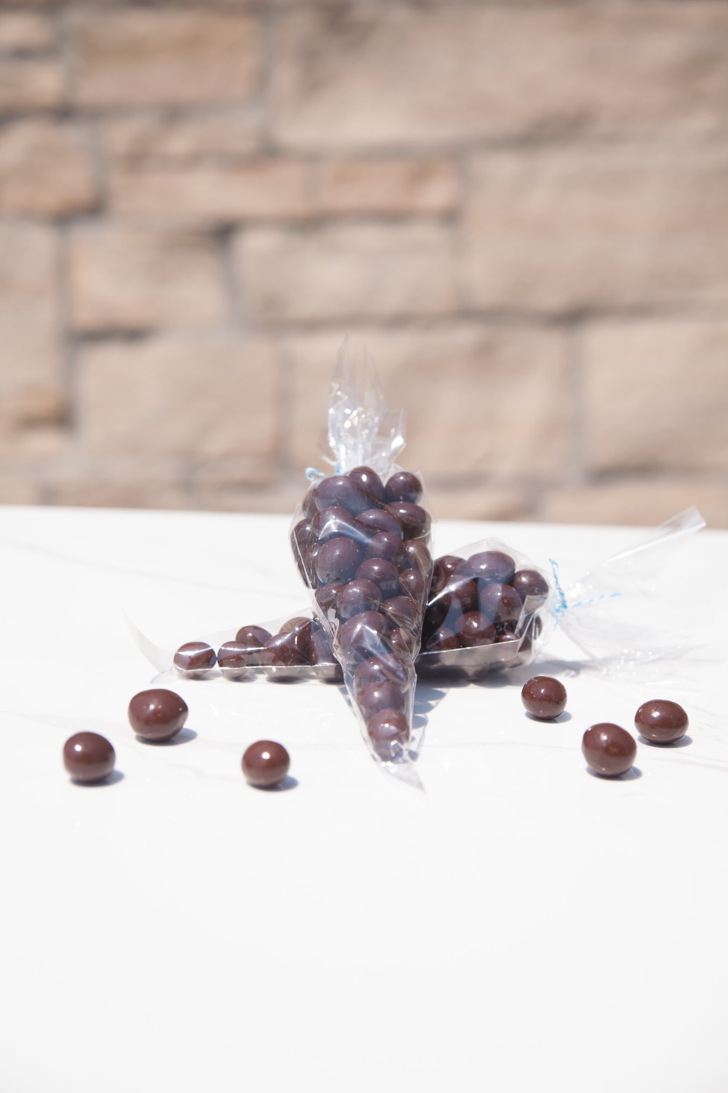 Cellophane cones of dark chocolate covered blueberries on a white counter, with loose berries scattered in front