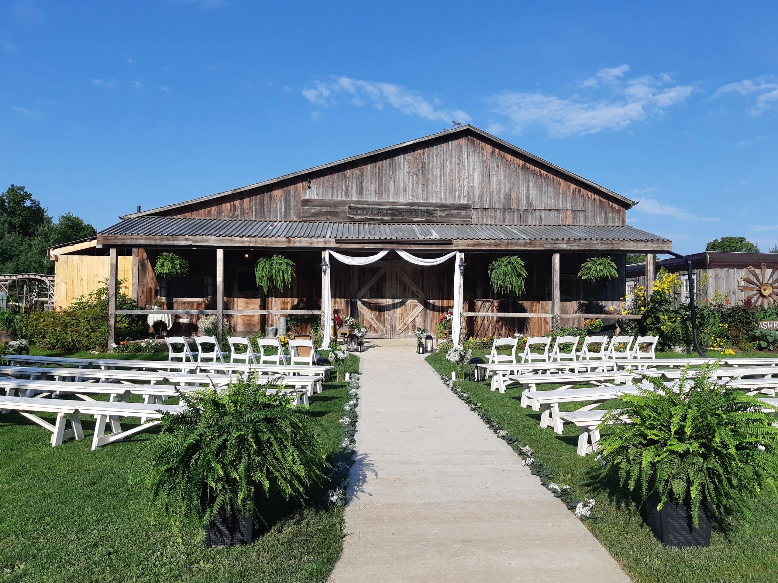 The weathered wooden Livery Stable barn with white benches and chairs set out on the lawn for a ceremony